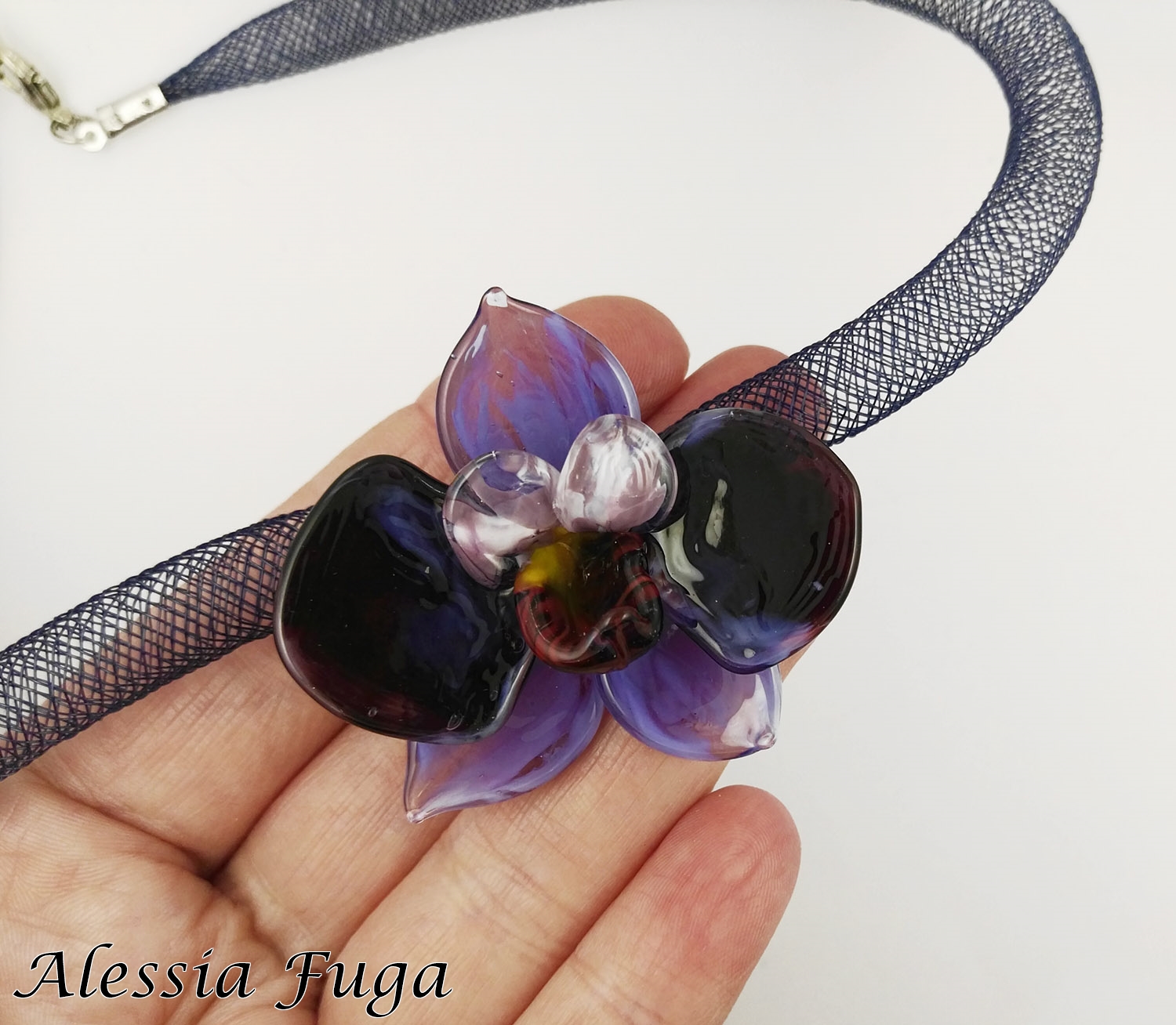 Lampwork wisteria orchlid pendant on a plastic mesh tube necklace in my hand for size reference